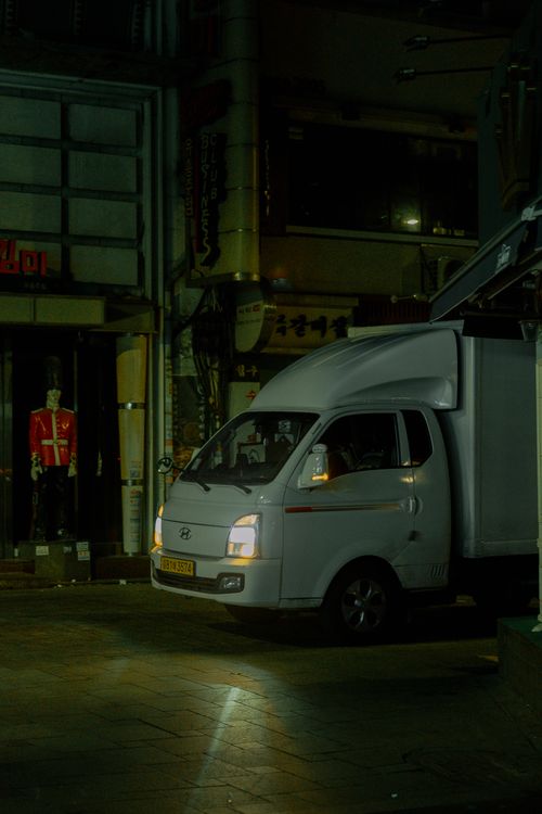 Free A white truck parked on a city street at night, surrounded by urban architecture and ambient lighting. Stock Photo