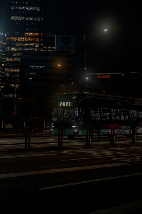 Free A city bus number 7021 traveling through urban streets at night with illuminated buildings. Stock Photo