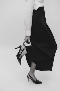 Sophisticated black and white fashion image of a woman adjusting her heeled shoe.