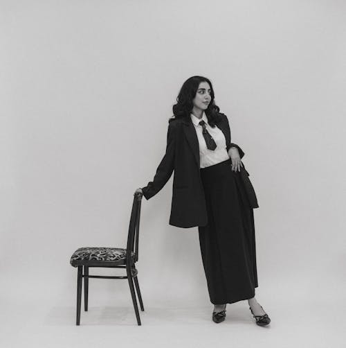 A woman in a suit and tie is standing next to a chair