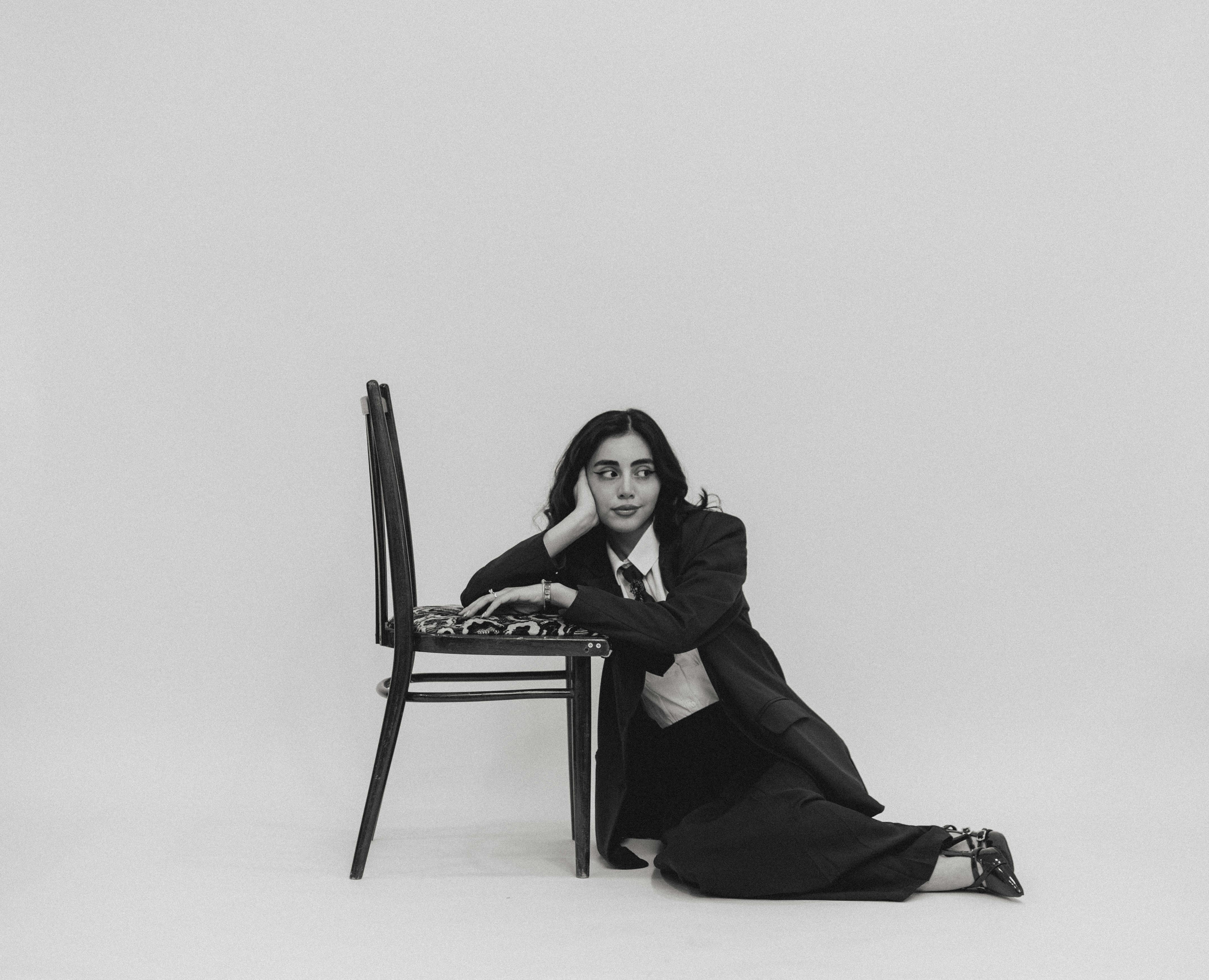 Elegant woman in suit sitting on the floor beside a chair in a studio.