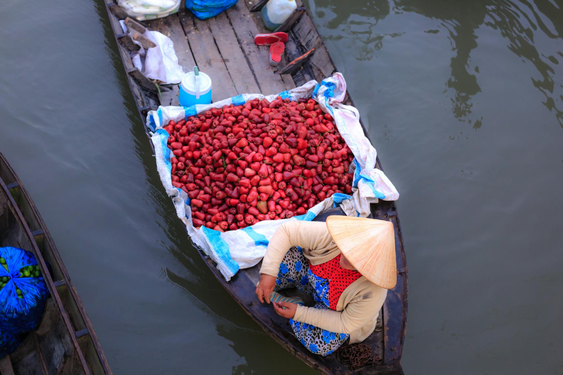 Asian woman sells vibrant fruits on a wooden boat in a lively floating market.