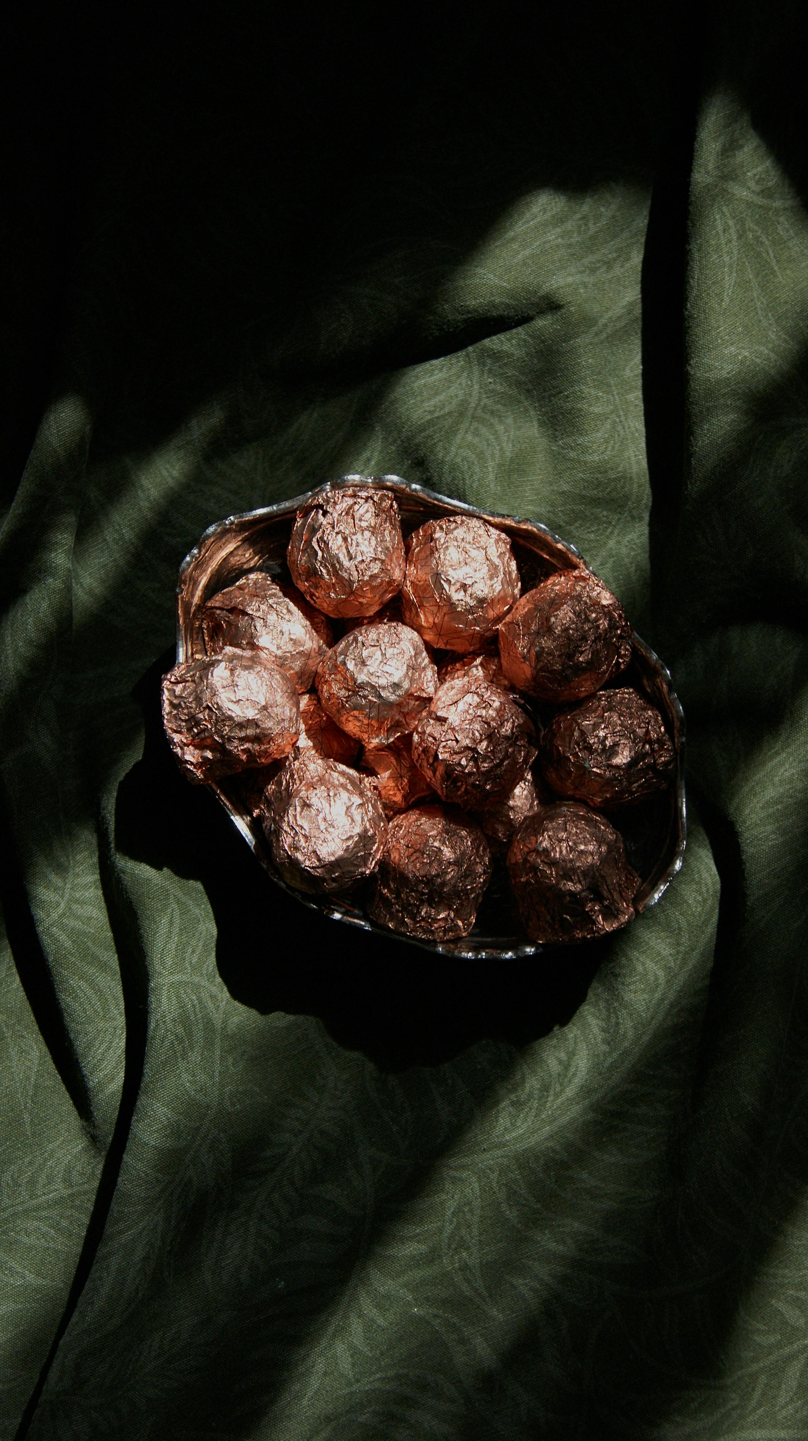 A bowl of foil-wrapped chocolates casting shadows on a green fabric, creating a moody atmosphere.