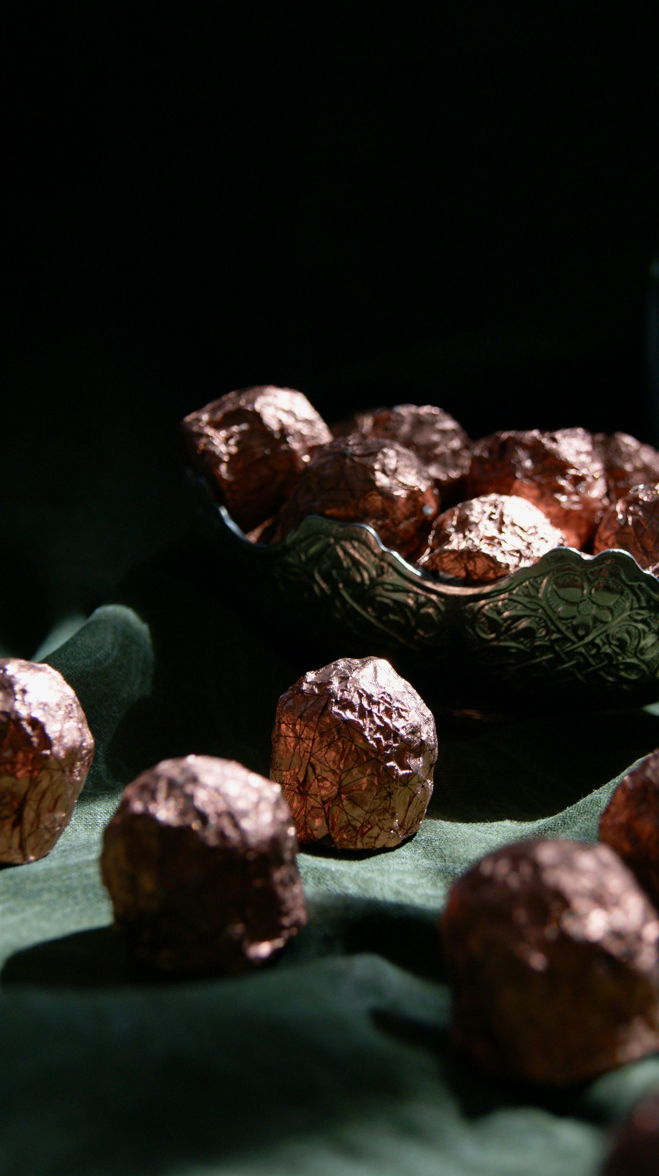 Luxurious dark chocolate truffles elegantly wrapped in foil, presented in a decorative bowl.