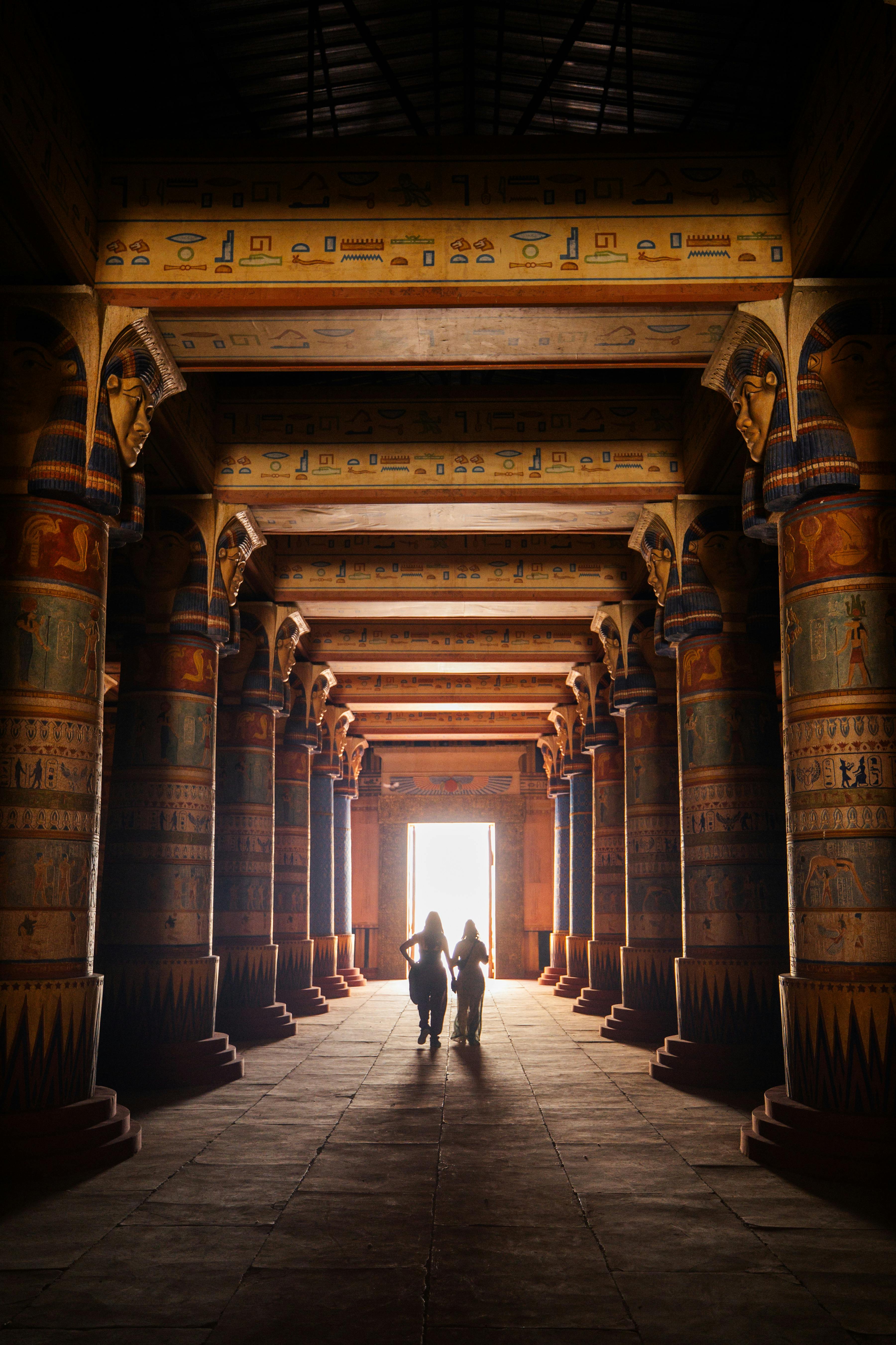 Two women walk through a historic temple adorned with carved columns, creating a sense of mystery and awe.