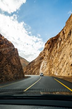 A car travels along a winding road through a rugged desert landscape under a bright blue sky.