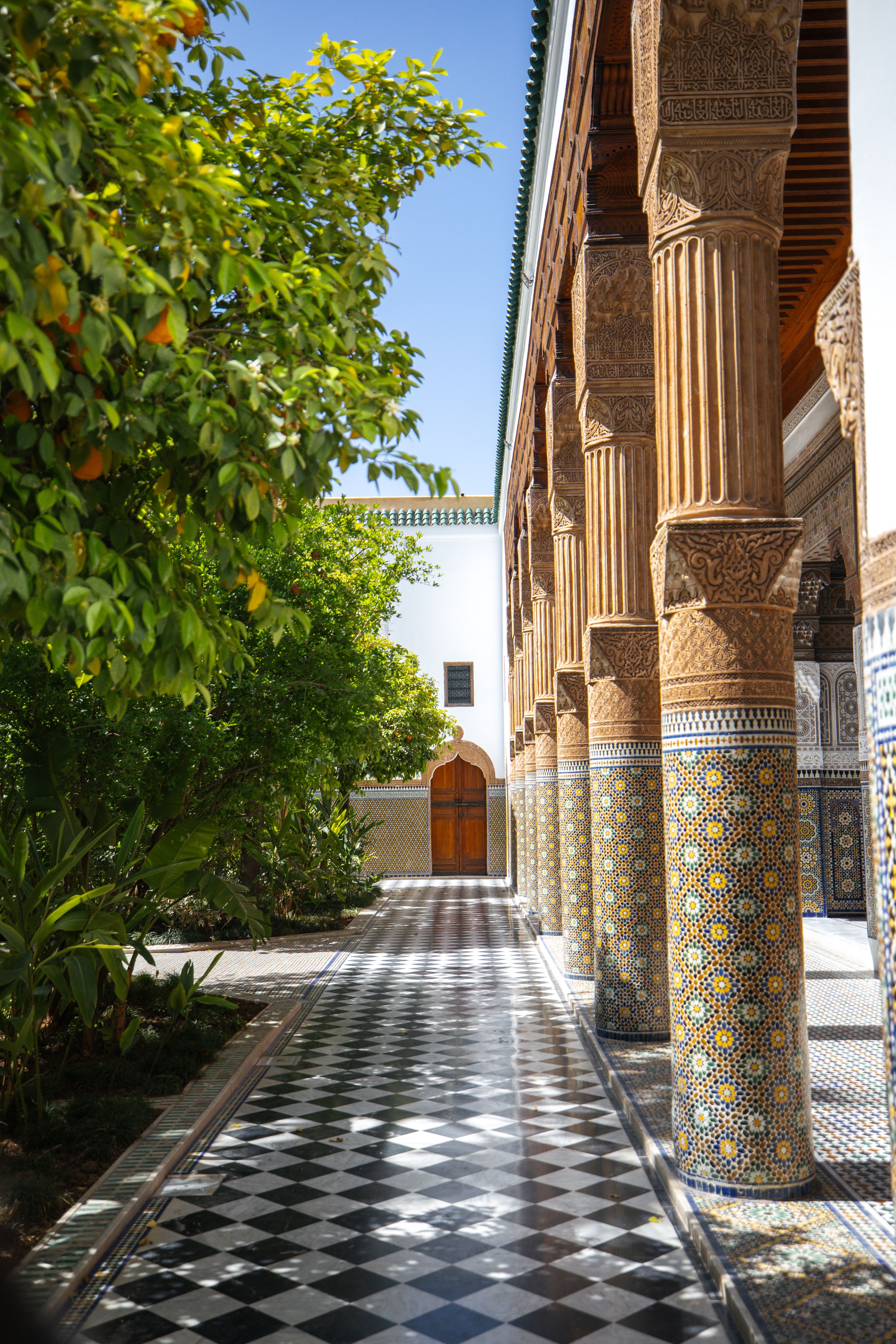 Sunlit Moroccan courtyard with intricate mosaic columns and lush greenery.