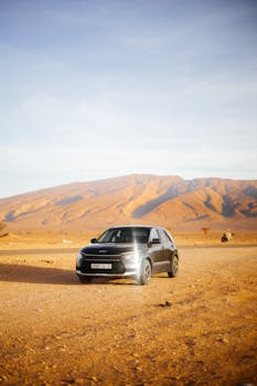 A sleek SUV drives through an expansive desert landscape with mountains in the background.