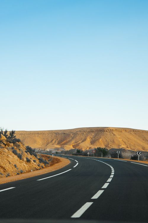 Free A winding desert road under a clear blue sky, ideal for travel and adventure themes. Stock Photo