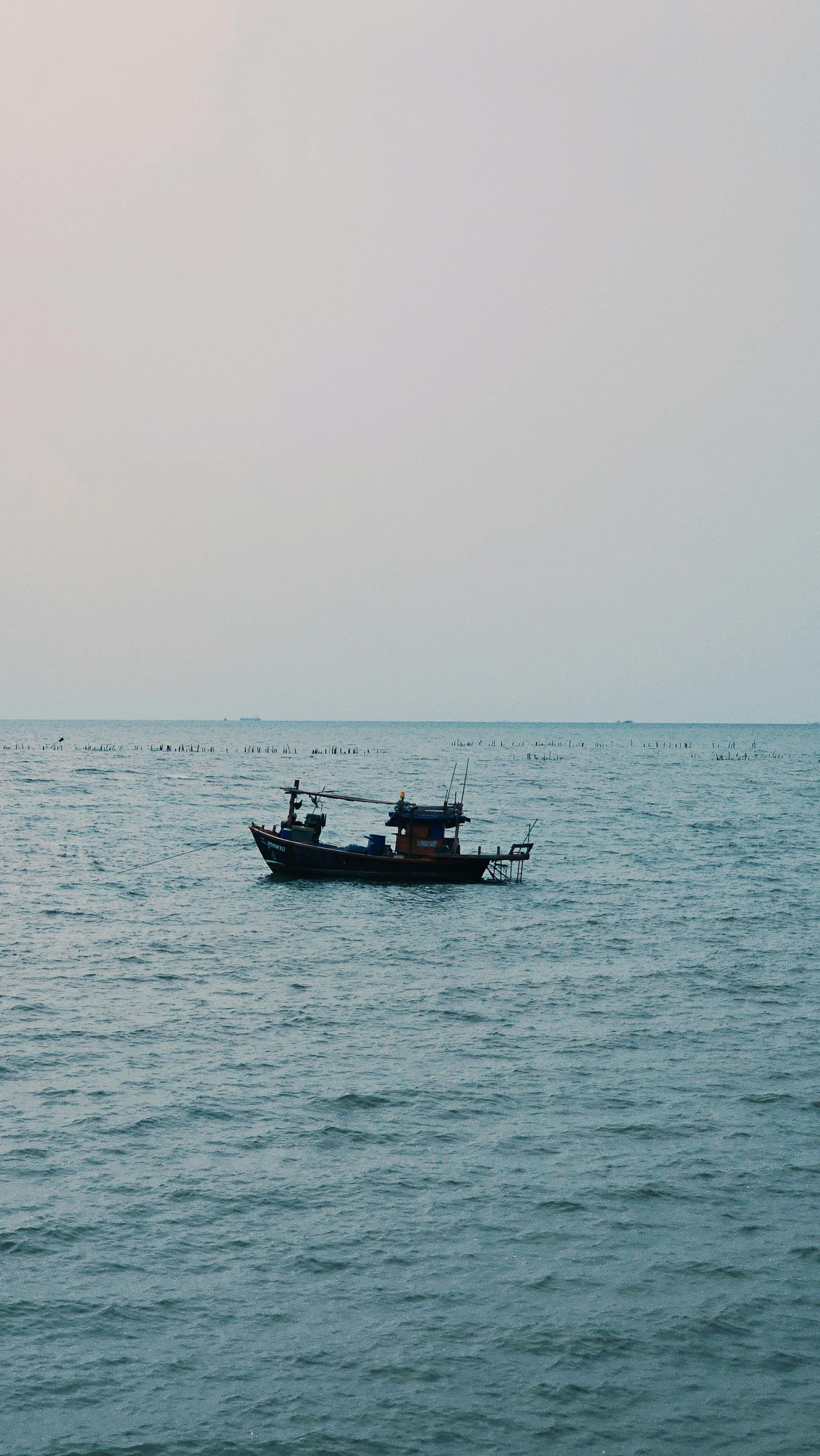 A lone fishing boat drifts on a calm sea under a soft sky, captured at dusk.
