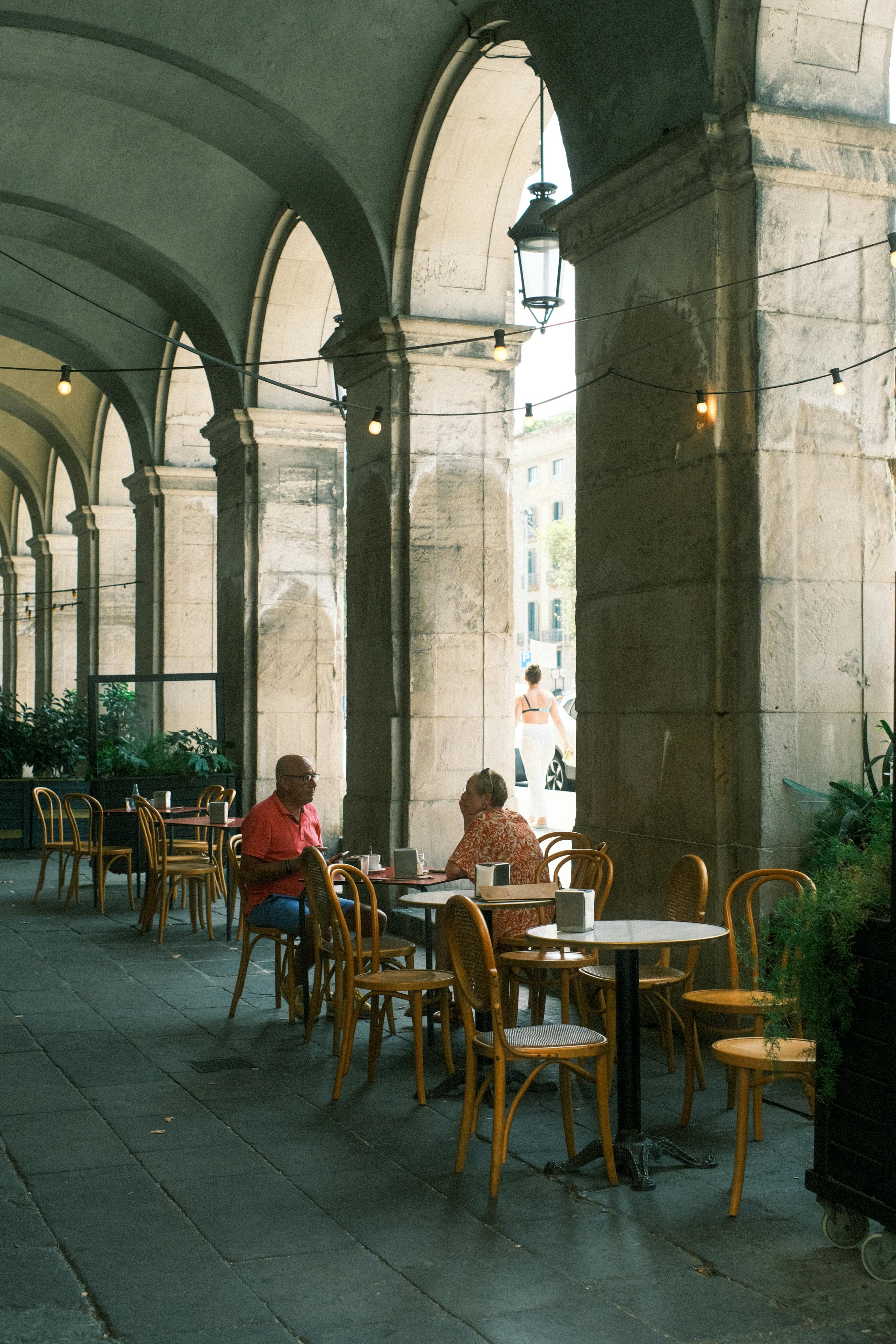 A cozy outdoor café setting under historical arches in Barcelona.