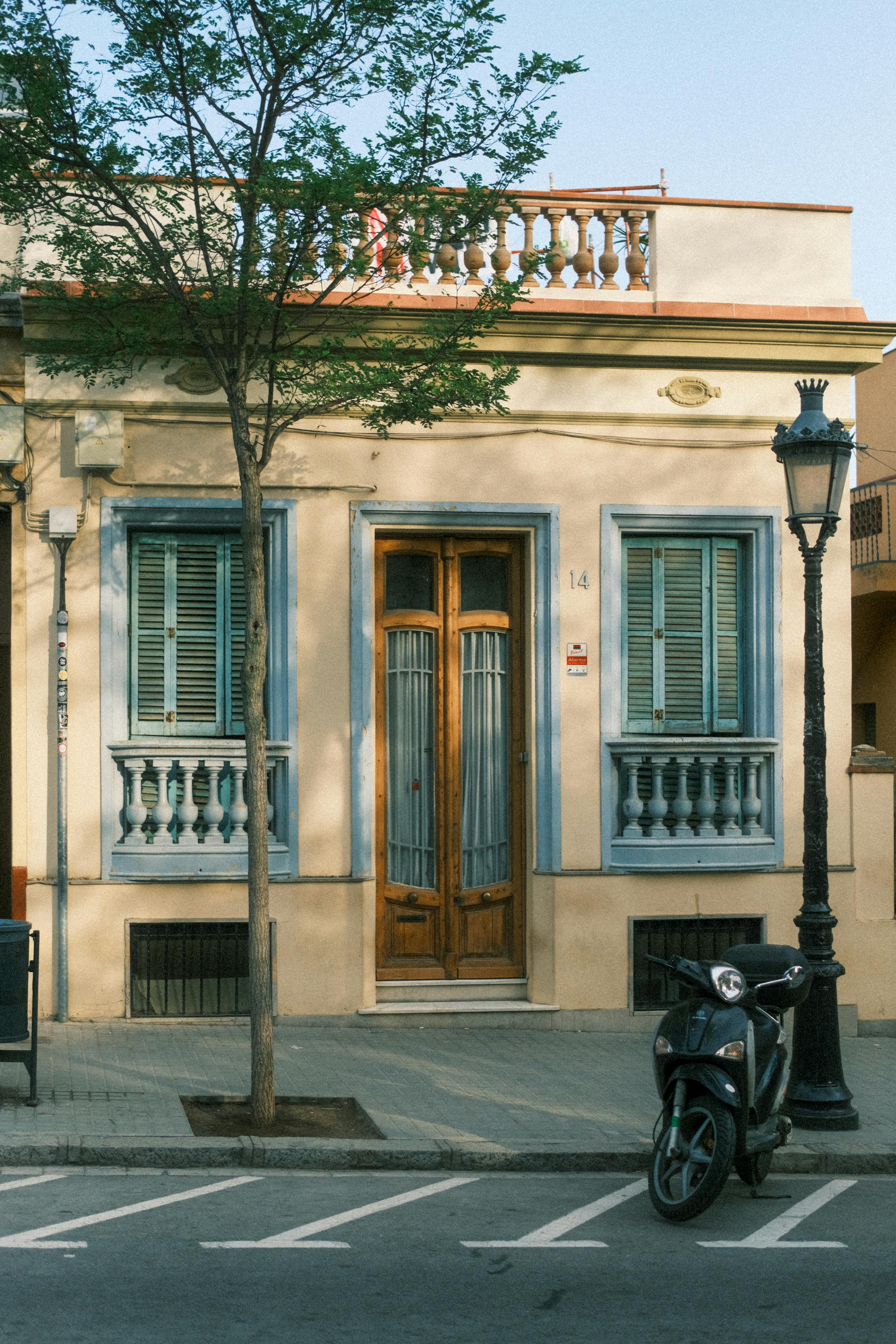 Elegant house facade in Barcelona, Spain with a parked motor scooter and tree-lined street.