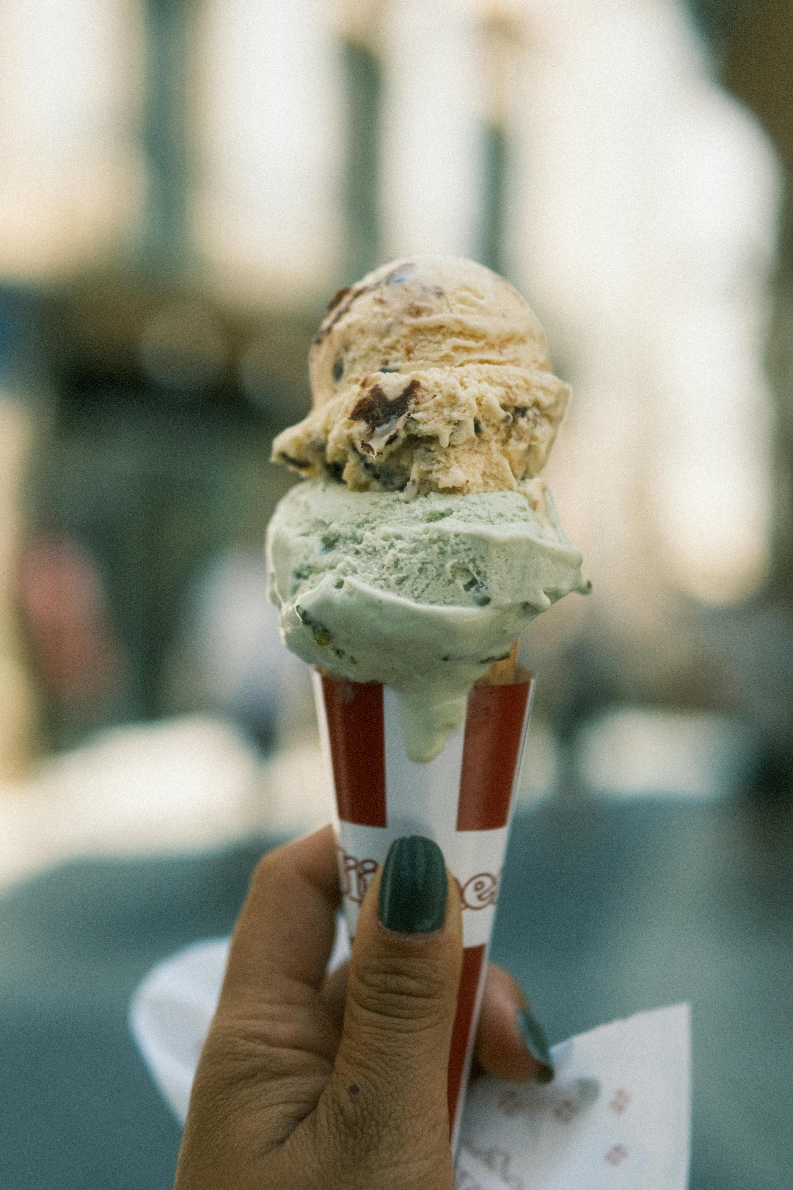 A close-up of a hand holding a double-scoop ice cream cone outdoors in Sitges, Spain.