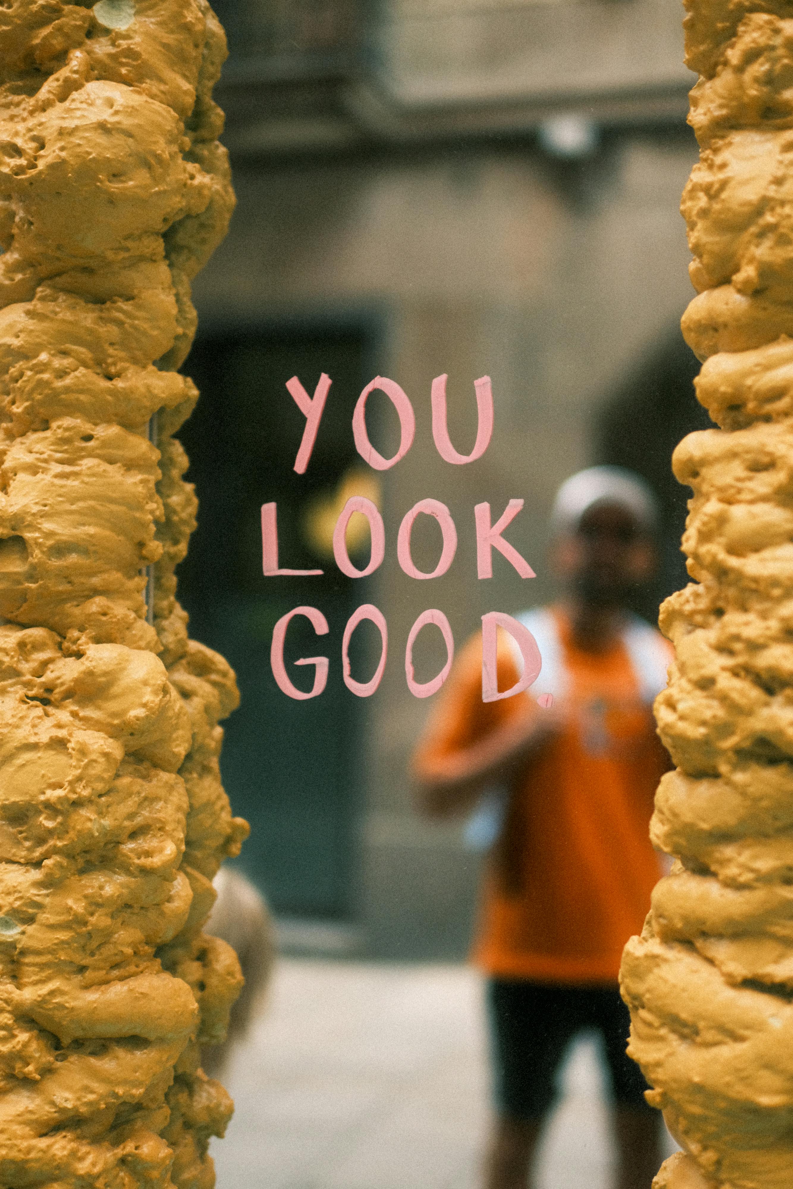 Man reflected in Barcelona mirror with 'You Look Good' text, surrounded by urban textures.