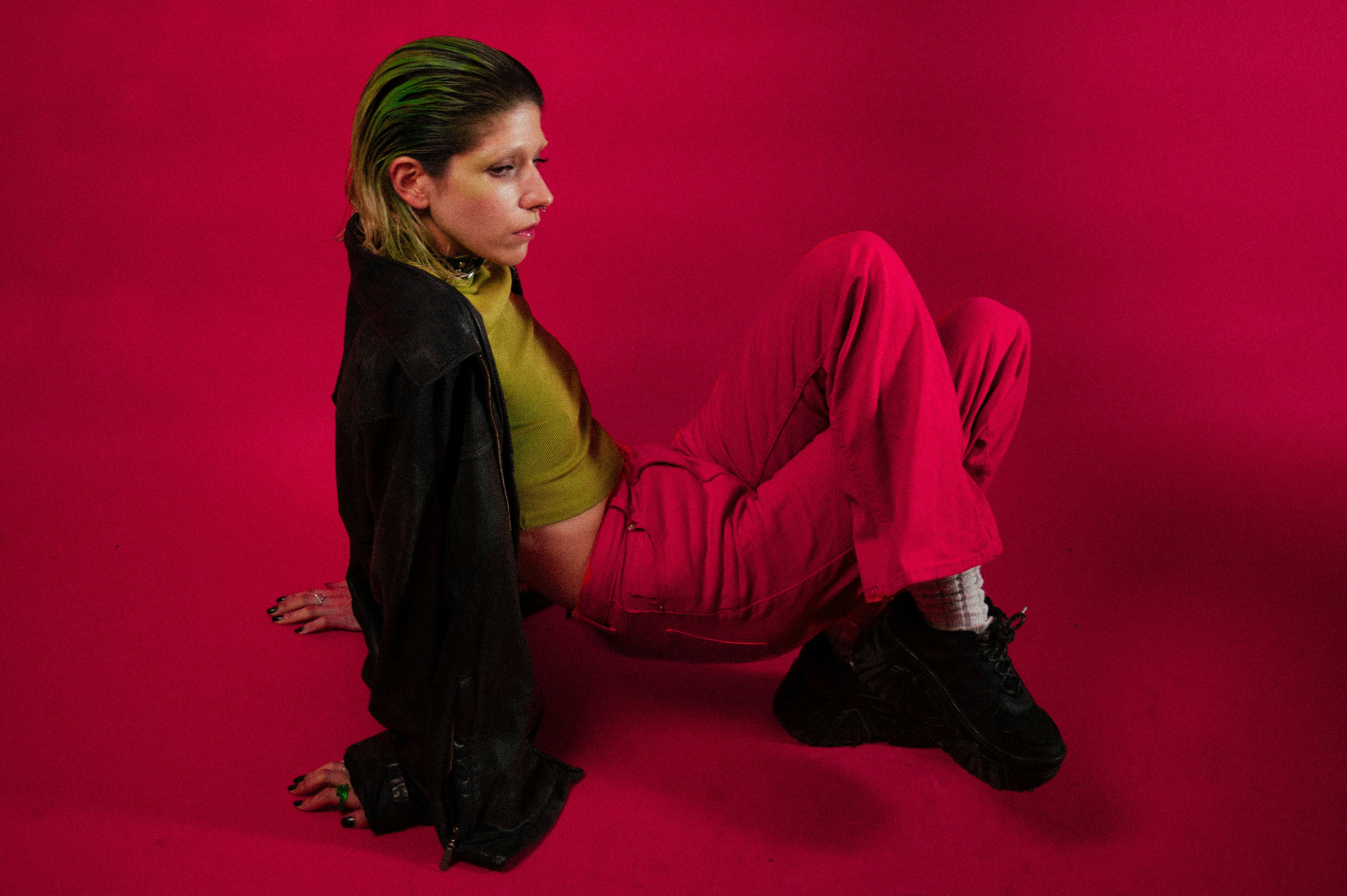 Free Fashion model in edgy attire poses against a vibrant red studio backdrop. Stock Photo