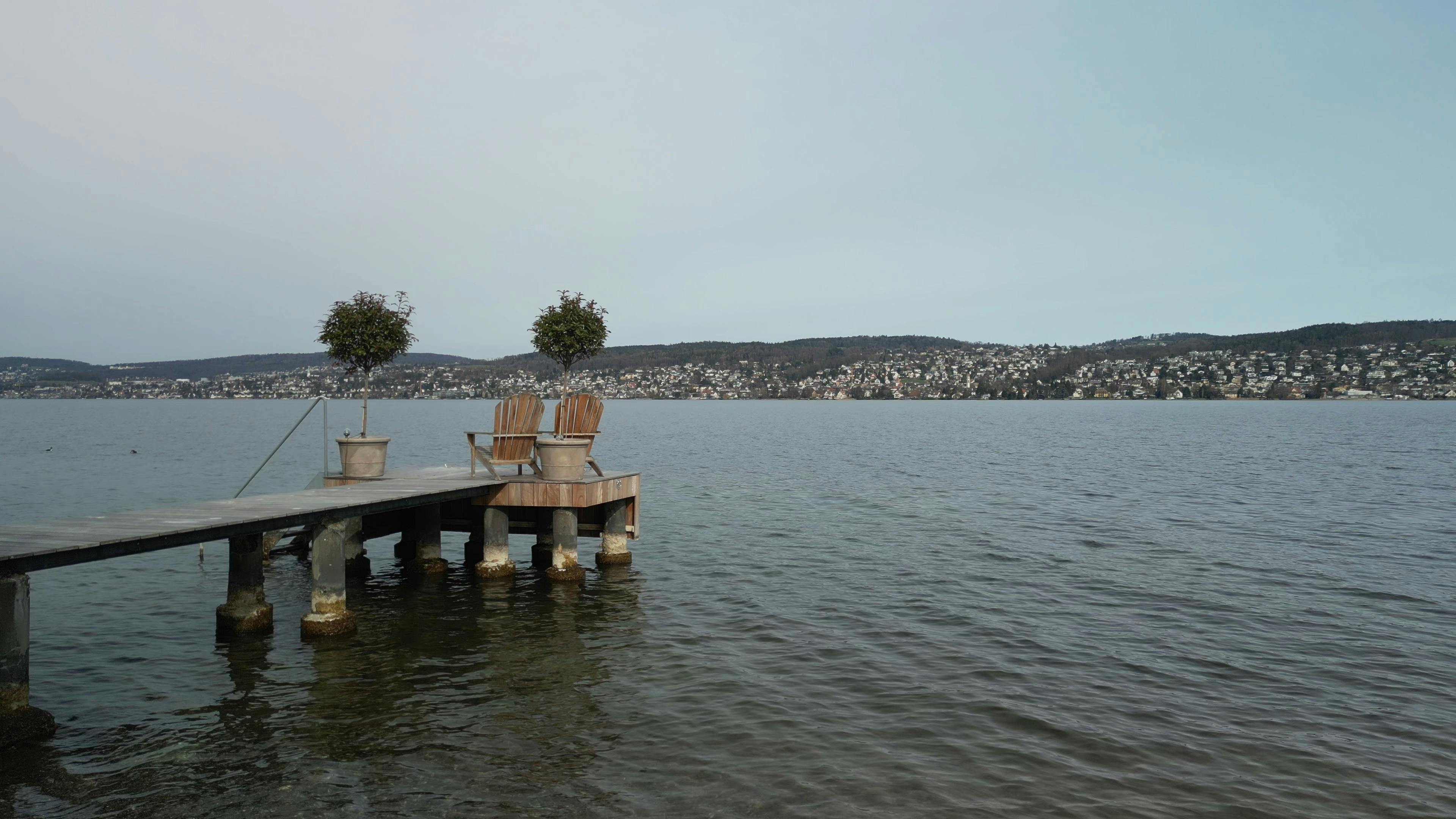 Peaceful pier on Lake Zurich with chairs and potted trees, ideal for relaxation.