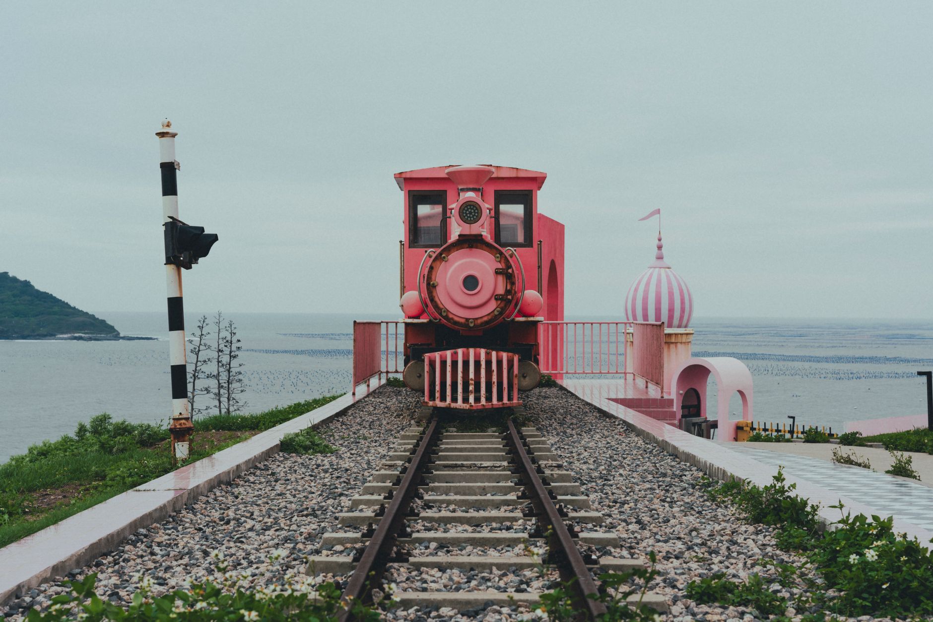 A charming pink vintage train on tracks by the sea, evoking nostalgia and travel allure.