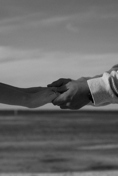 Free Intimate black and white image of a couple holding hands at the beach. Stock Photo