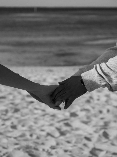 Free Black and white photo of a couple holding hands on a serene sandy beach, showcasing love and togetherness. Stock Photo