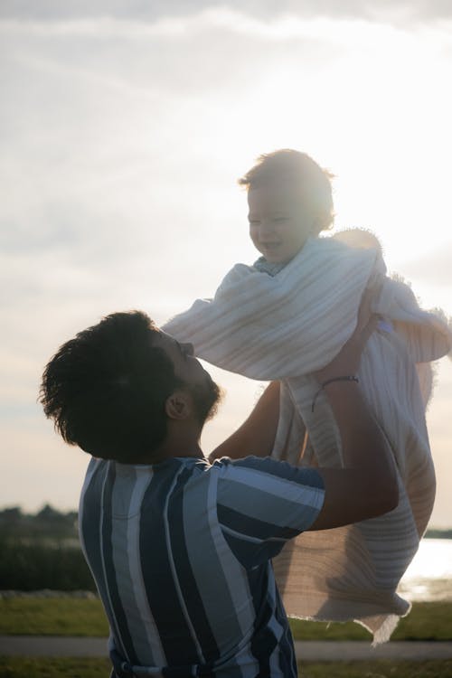 A man holding a baby in the air at sunset
