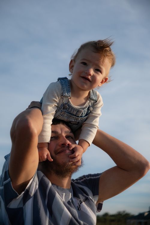 Free A joyful moment of a father carrying his smiling son on his shoulders outdoors. Stock Photo