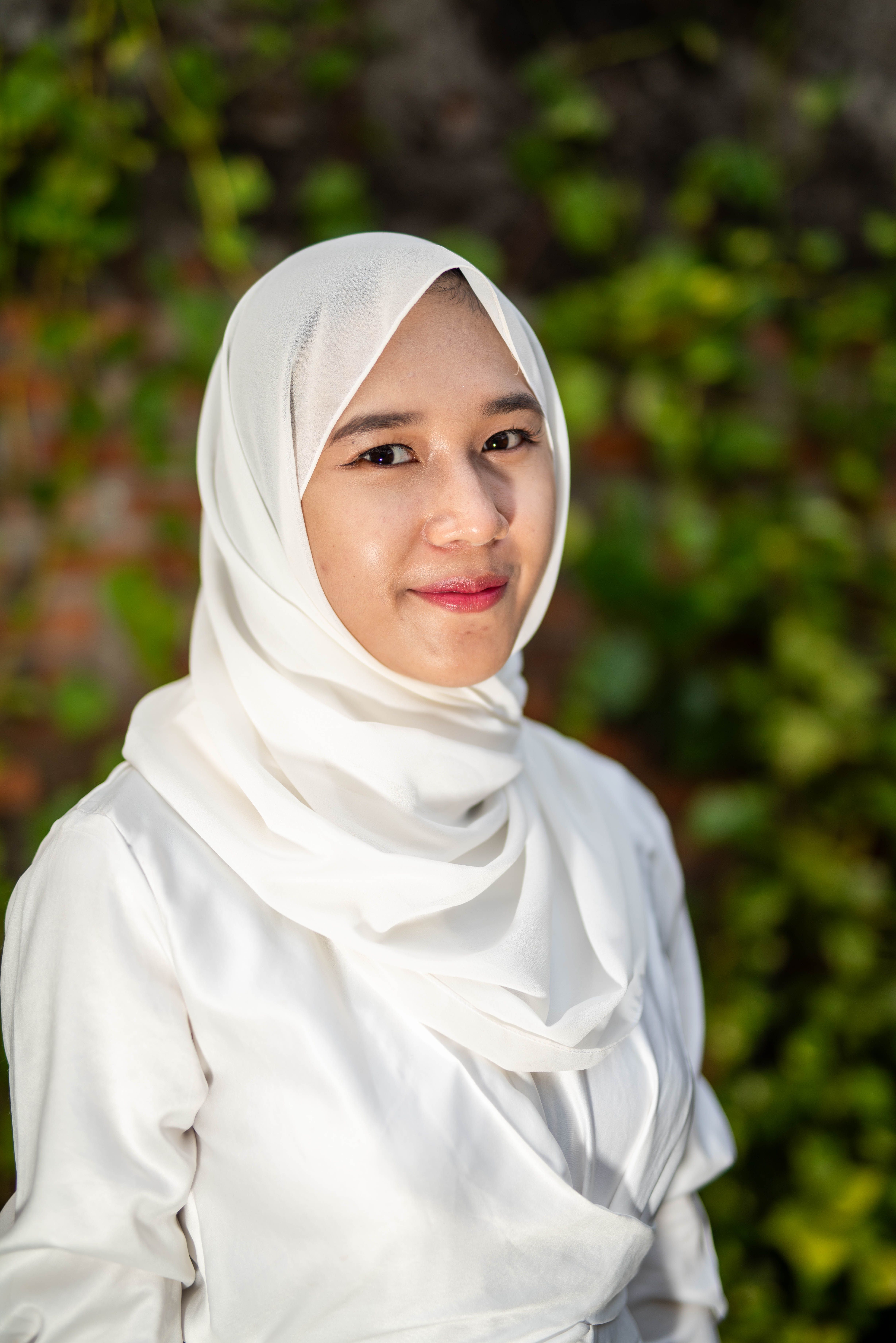 Charming portrait of a woman wearing a white hijab, captured with vibrant greenery in the background.