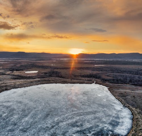 A sunset over a frozen lake in the middle of a field