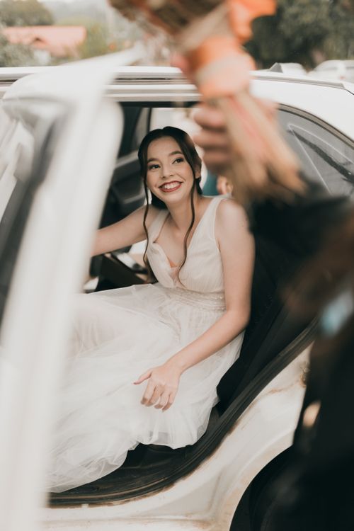 Free A joyful bride smiles while sitting in a car, wearing a beautiful wedding dress. Stock Photo