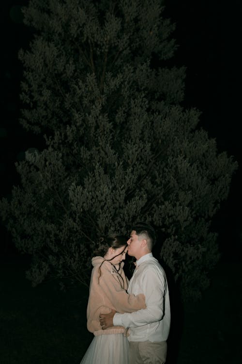 Young Couple Embracing Next to Tree at Night