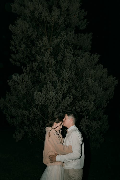 Free Young Couple Embracing Next to Tree at Night Stock Photo