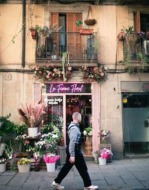 A man walking down a street with flowers in front of a flower shop