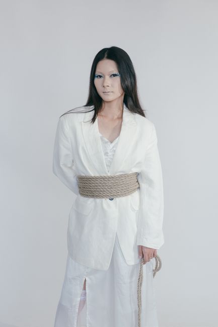 Fashion portrait of a woman in a white blazer tied with rope, studio setting.