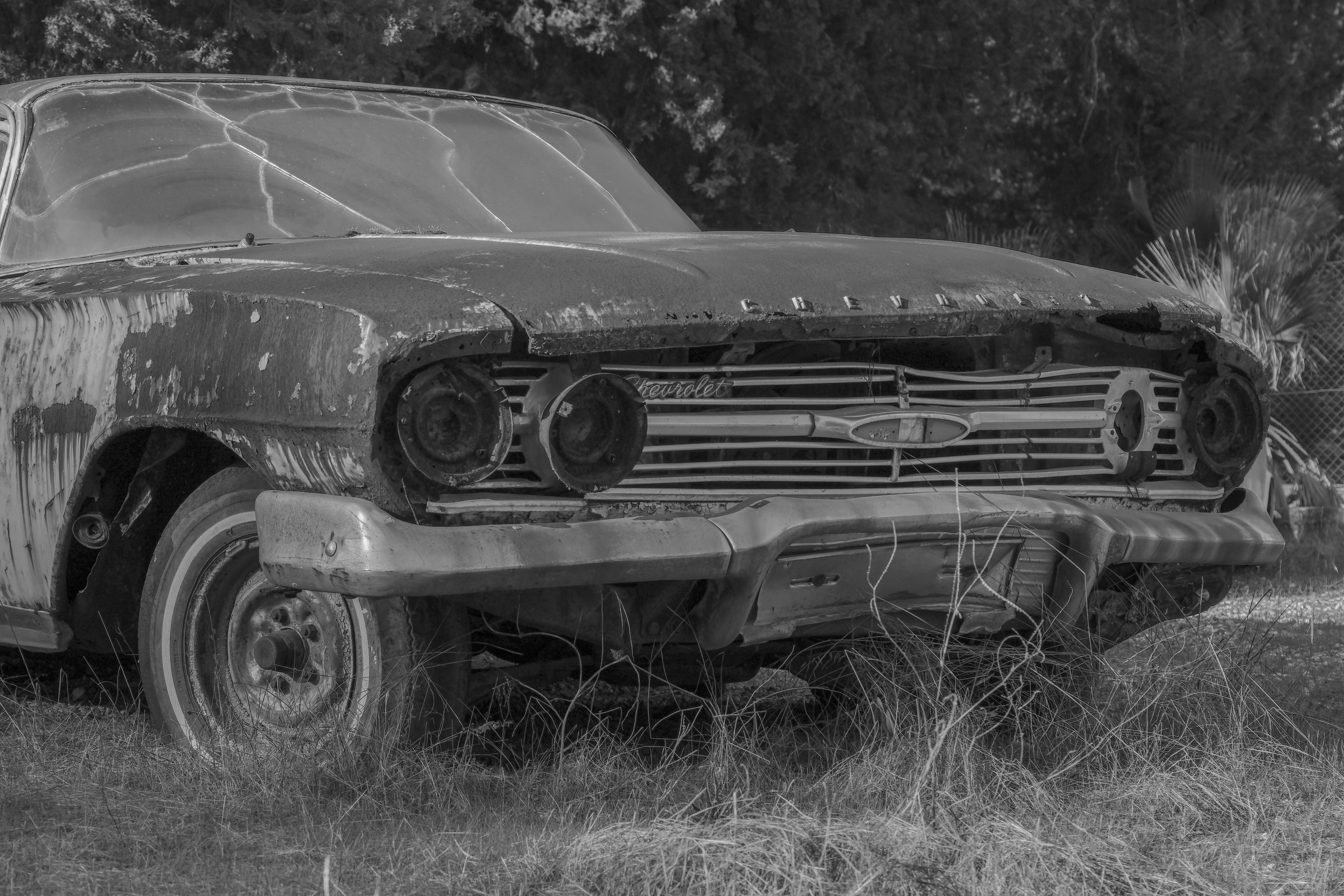 Black and white photo of an abandoned rusty car in grassy field, Dalaman.