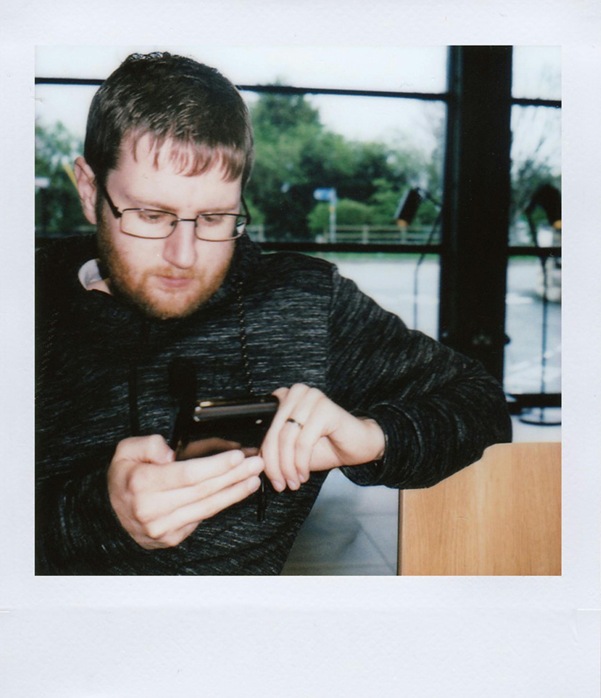 Portrait of a man with glasses focused on using his smartphone indoors.
