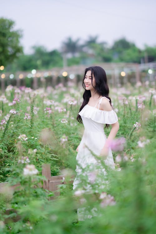 A woman in a white dress is standing in a field of flowers