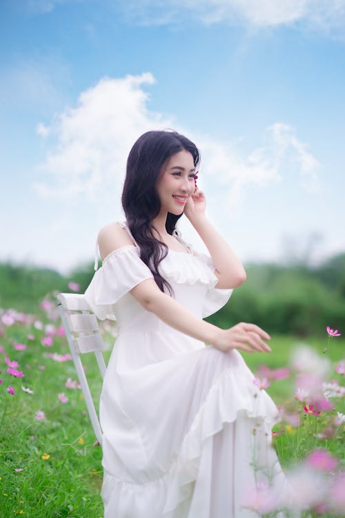 A woman in a white dress sitting on a chair in a field