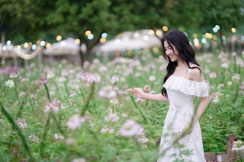 A woman in a white dress is walking through a field of flowers