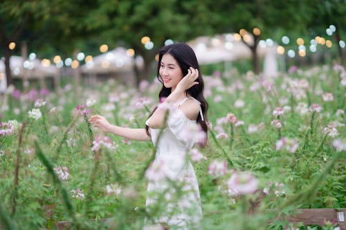 A woman in white dress is walking through a field of flowers