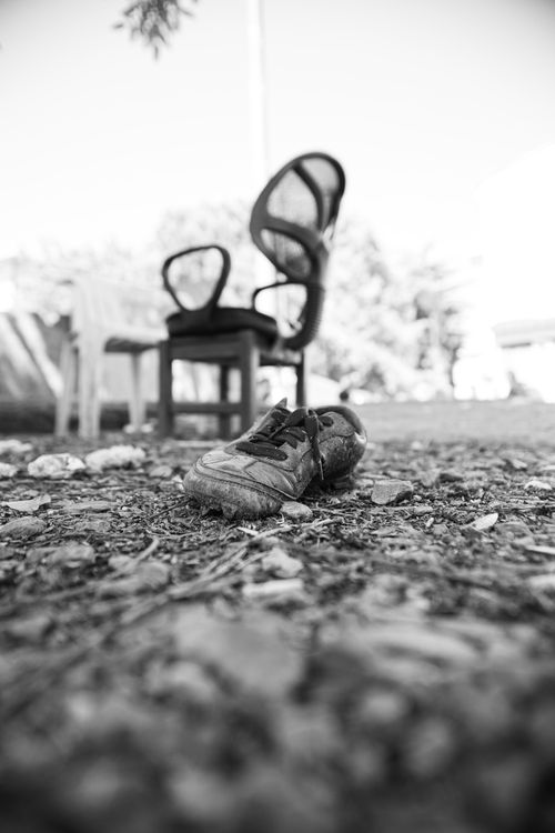 Free A black and white image of an abandoned shoe and chairs on a rough surface, evoking a sense of neglect. Stock Photo