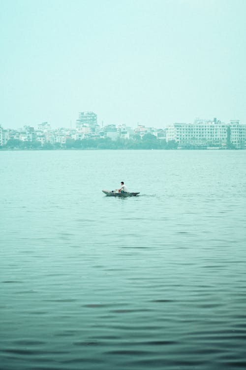 A man is sitting in a small boat on the water