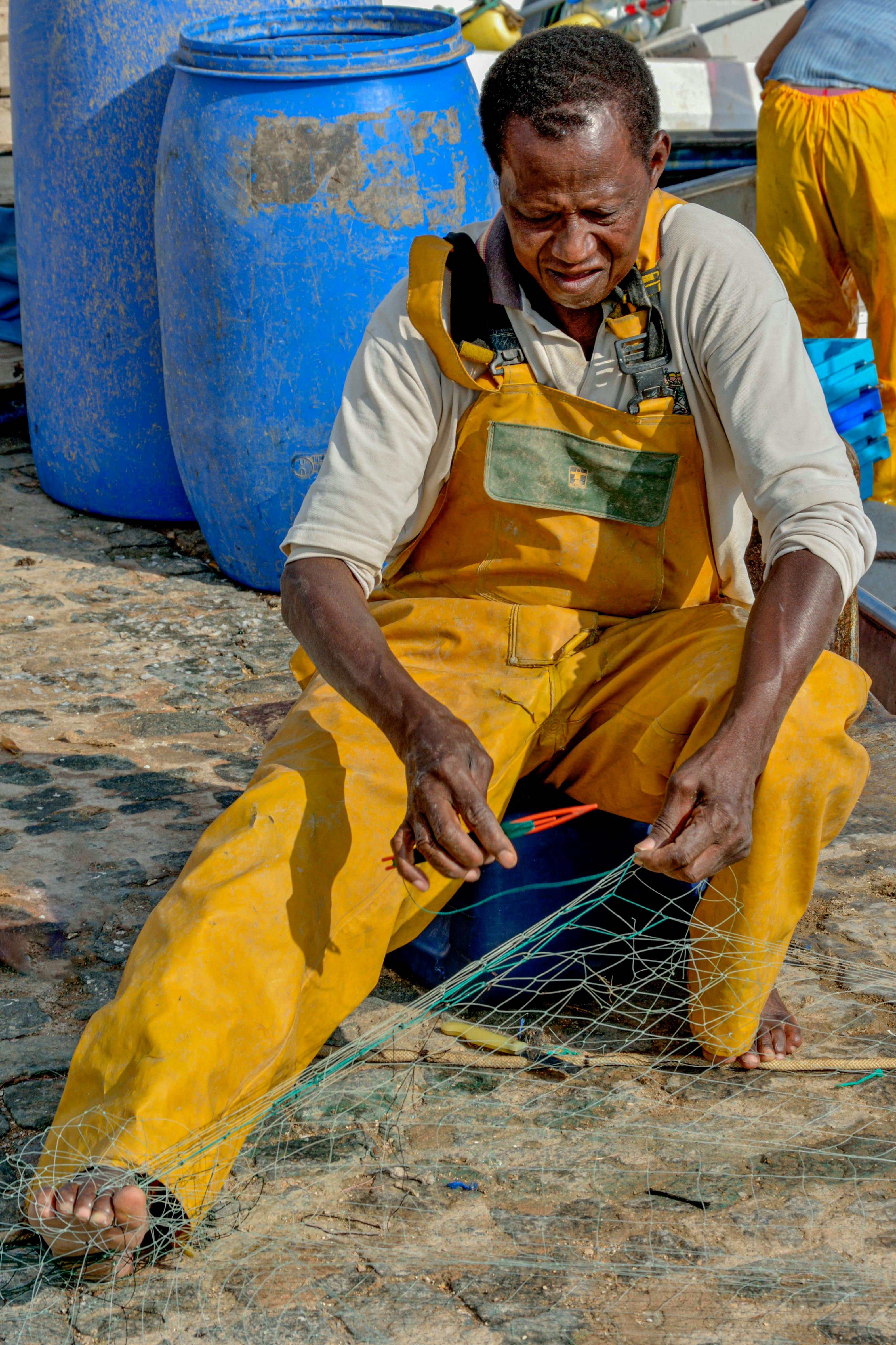 A skilled fisherman in Cartagena, Spain, repairs a net wearing yellow bib overalls, displaying traditional craftmanship.