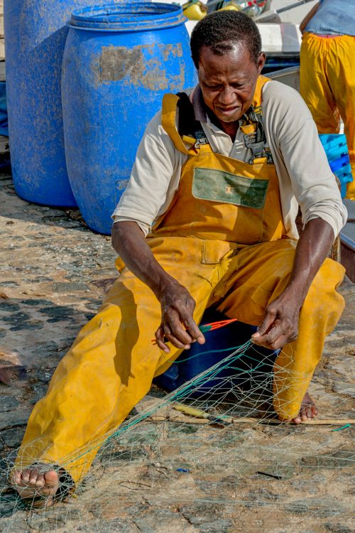 Free A skilled fisherman in Cartagena, Spain, repairs a net wearing yellow bib overalls, displaying traditional craftmanship. Stock Photo
