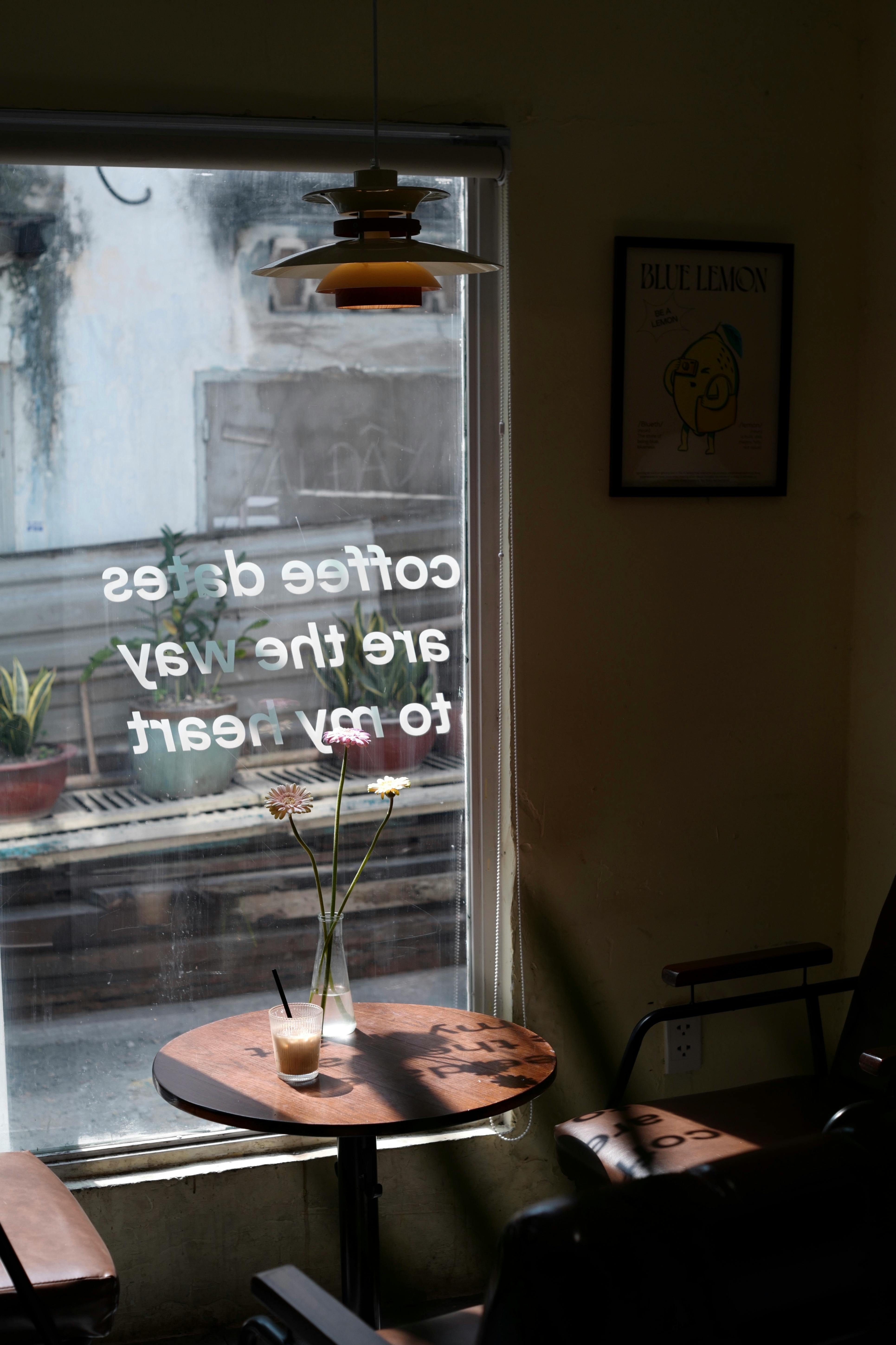 Cozy coffee shop window scene with a drink and flowers on a table.