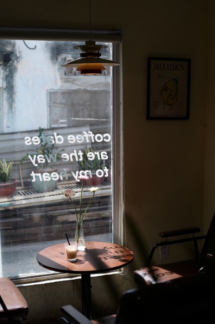 Cozy coffee shop window scene with a drink and flowers on a table.