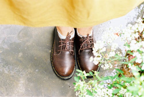 A person wearing brown shoes standing in front of flowers