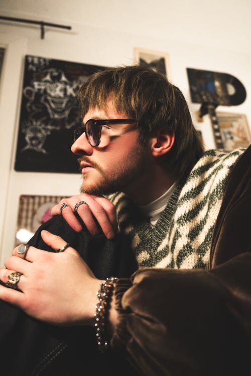 A man with glasses and a necklace sitting in front of a mirror