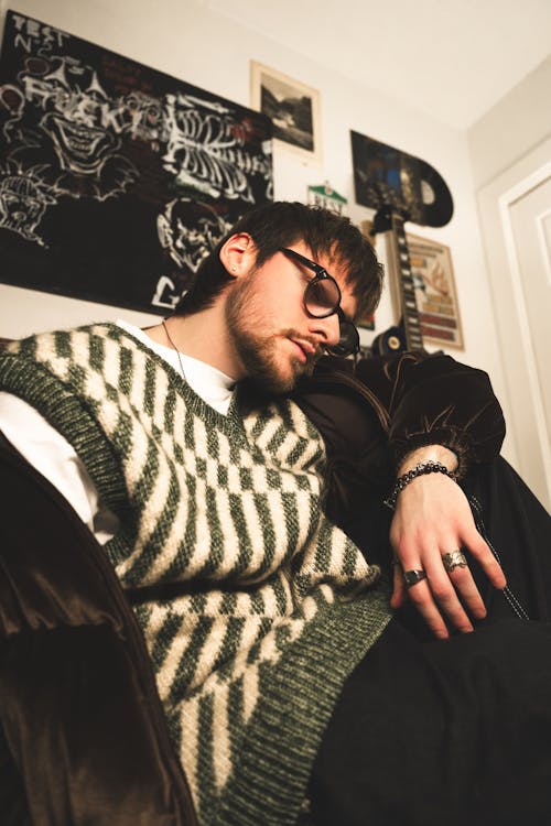 A man with glasses and a sweater is sitting on a couch