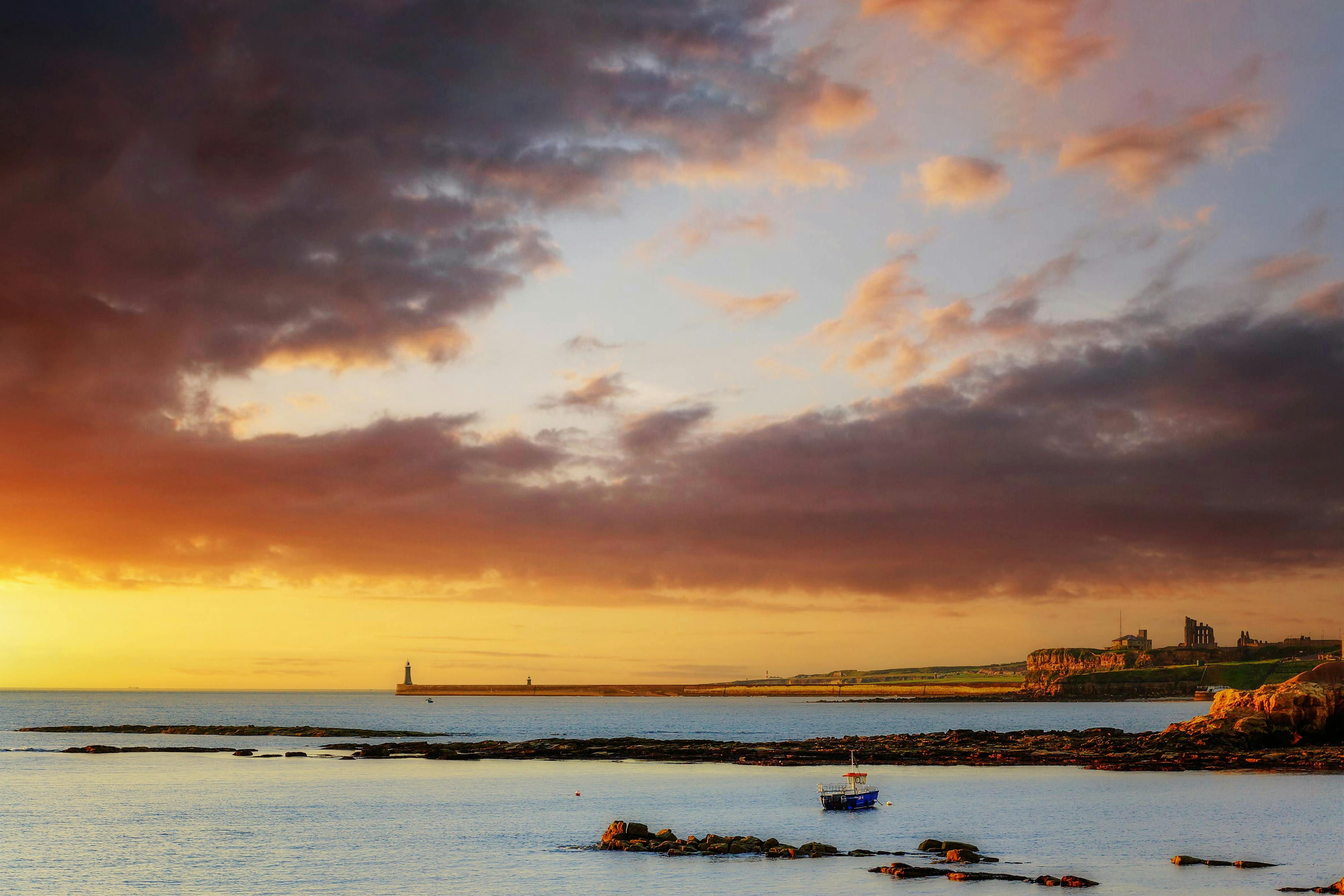 Beautiful sunset over Tynemouth Priory and Lighthouse with dramatic clouds and calm sea.