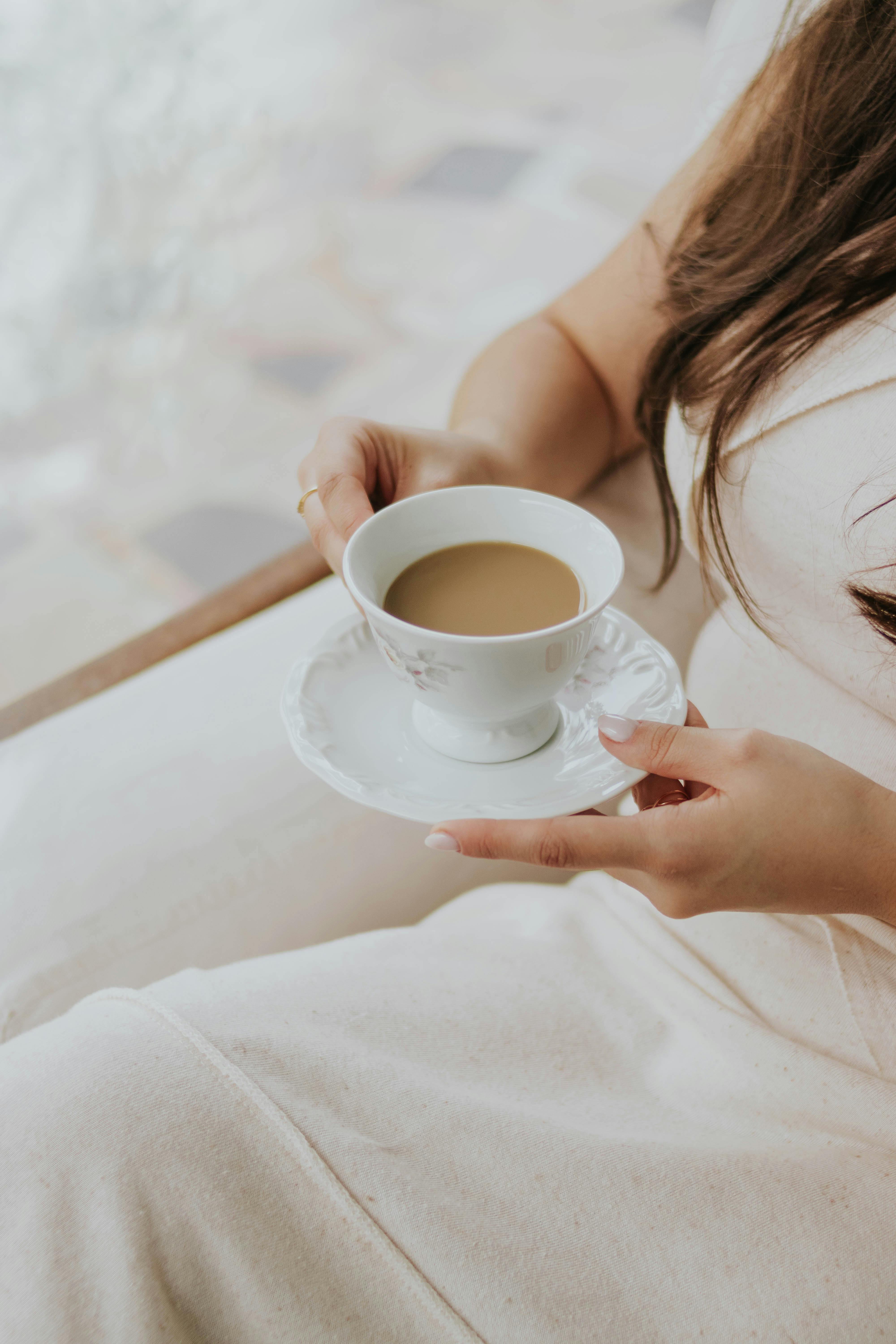 Close-up of a woman holding a coffee cup with a saucer, creating a calm atmosphere.