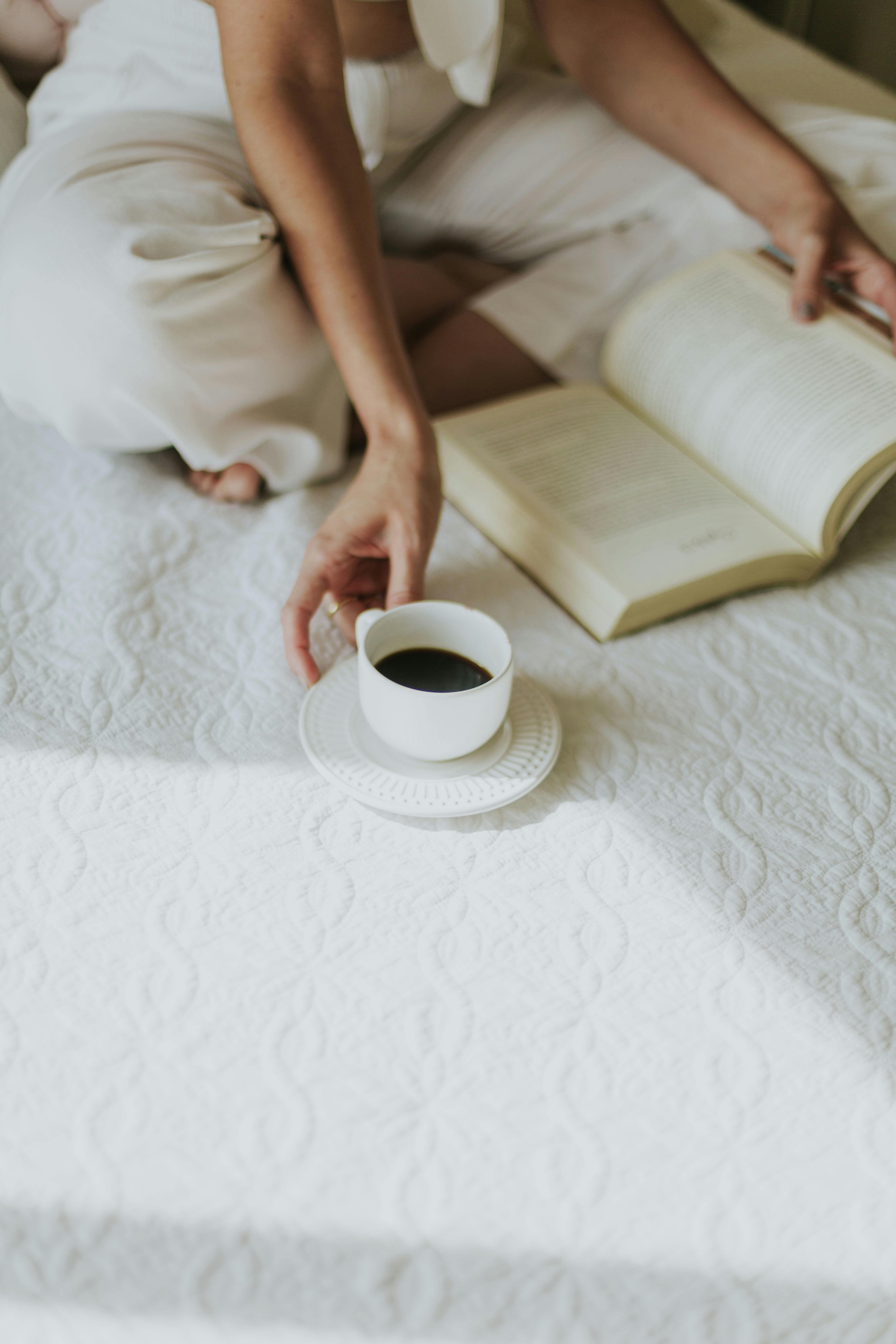 A woman enjoys a peaceful morning, reading with coffee on a cozy bed.